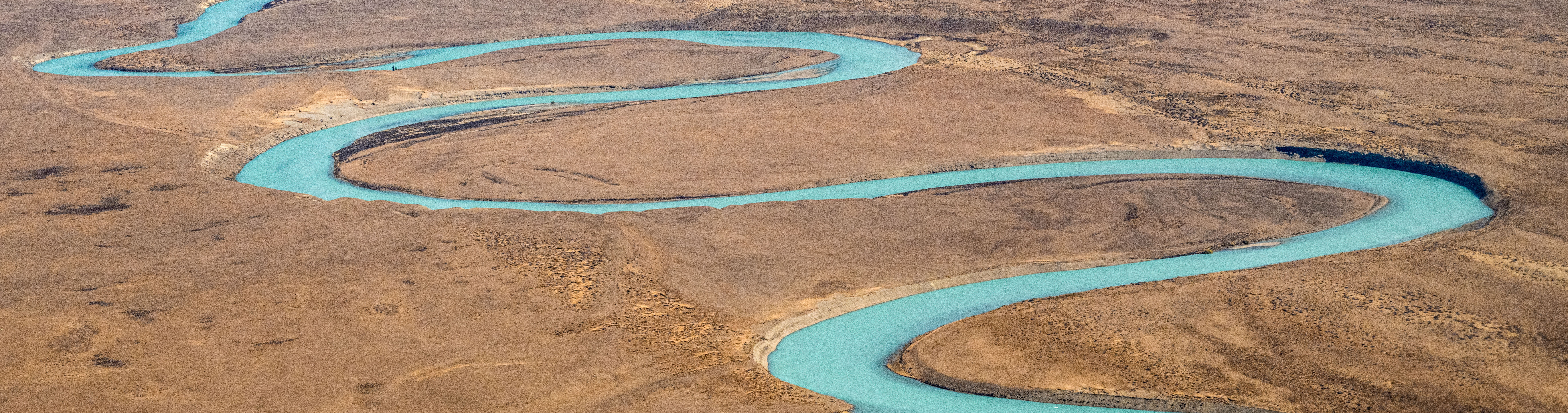 The meandering turquoise river contrasts a golden sedimentary landscape