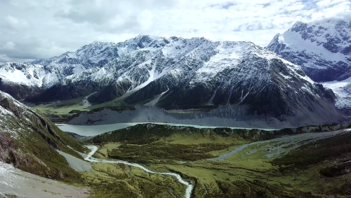 A snow capped mountain range above a green glacially carved valley.
